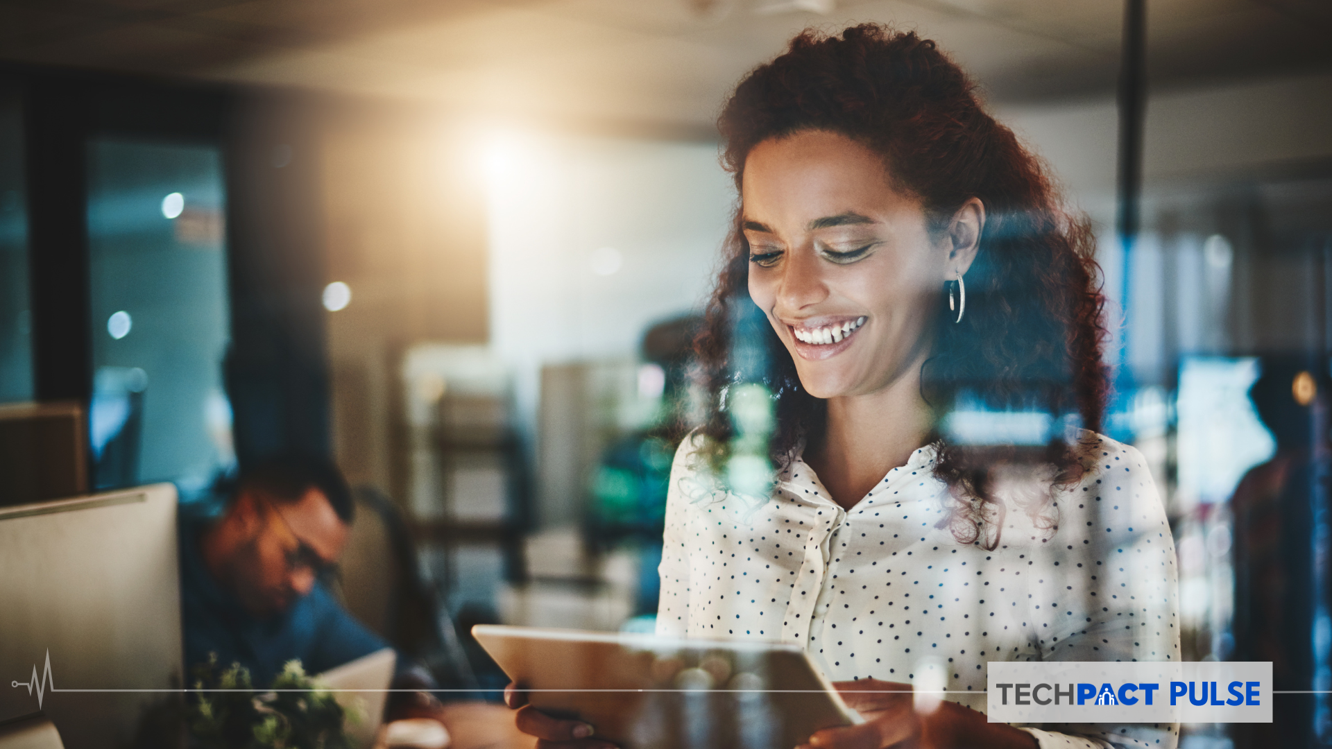woman smiling at a tablet in an office in the evening with office light on