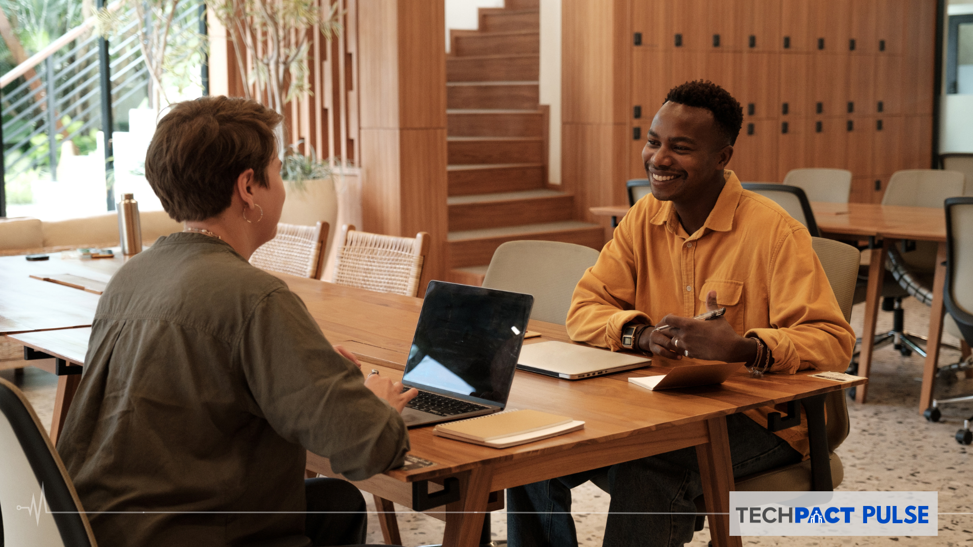 A young Black man sitting across an middle aged White woman on a table who has a laptop open